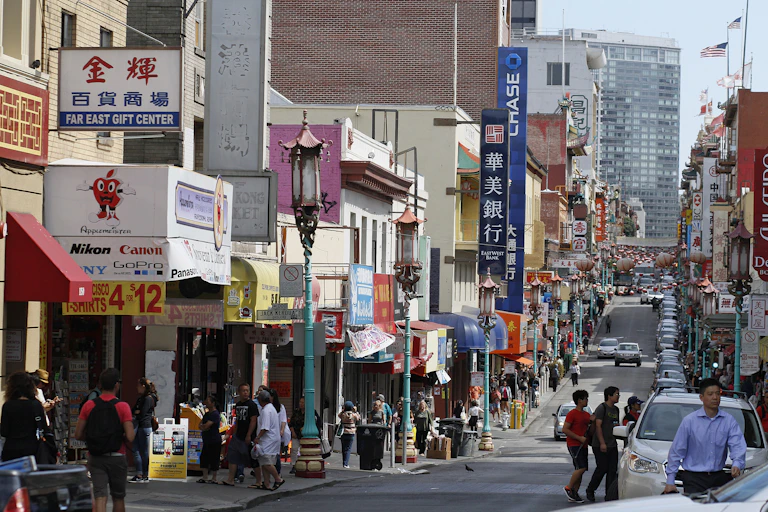 People walking down the sidewalk of a downtown street, with Chinese storefront signage