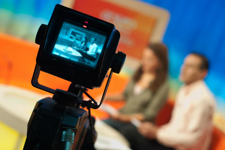 A camera is directed at two people sitting on a couch during a TV show