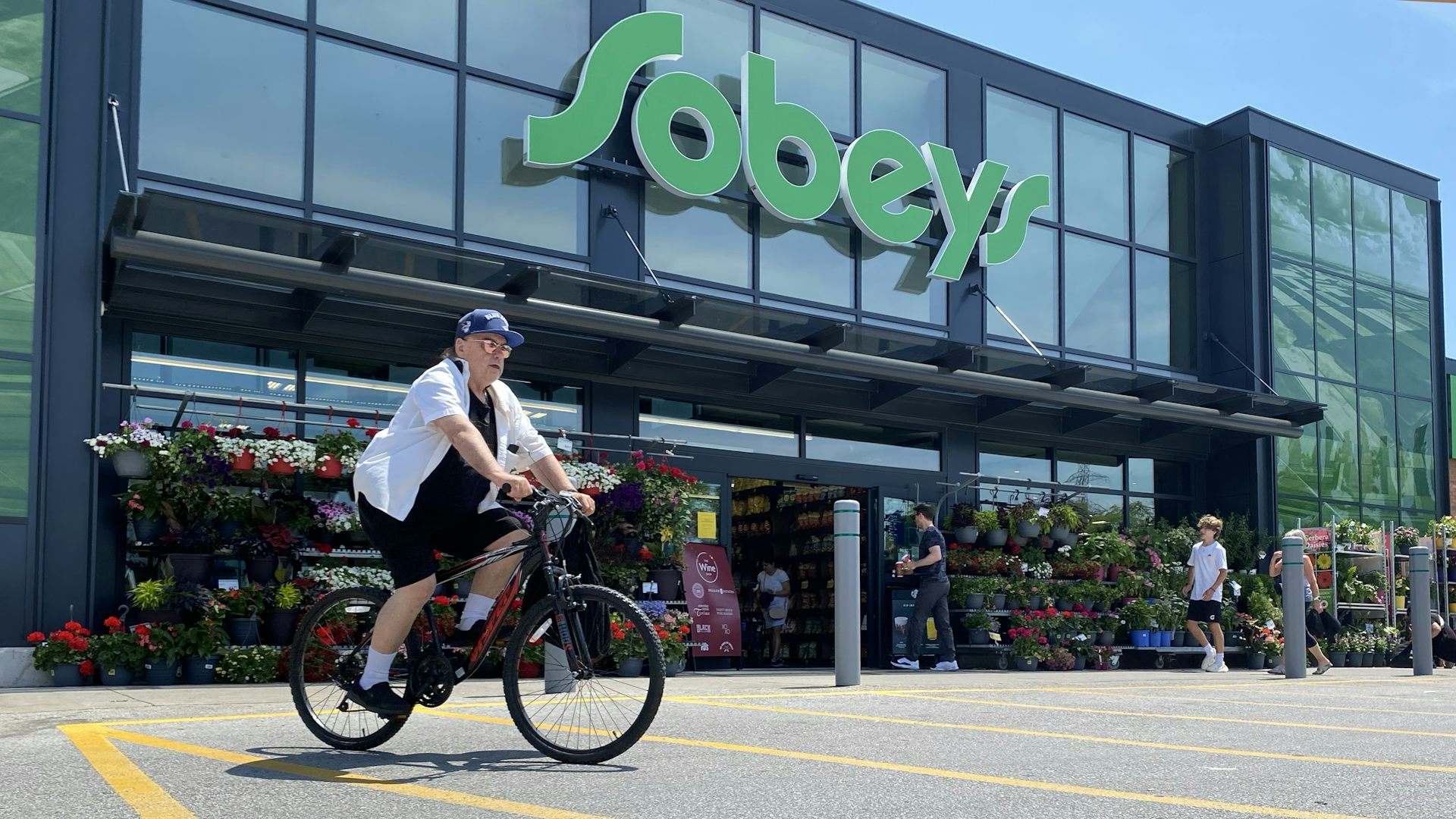 A person rides a bicycle in front of a Sobeys grocery store