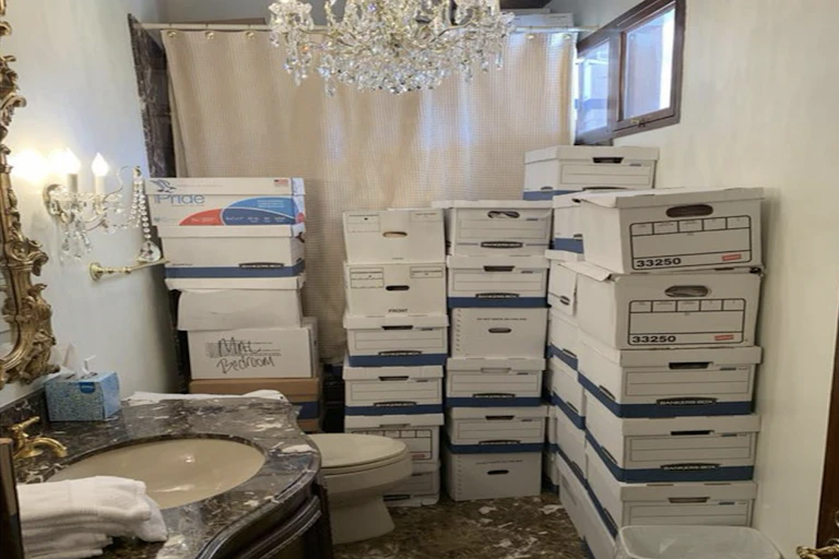 White boxes are stacked along a wall and tub of a bathroom.