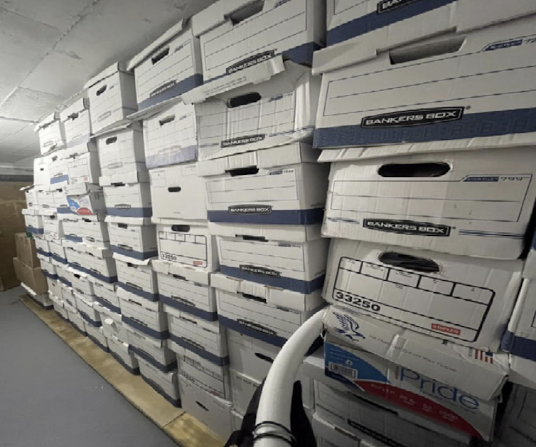 Bankers boxes are stacked ceiling high against a wall.