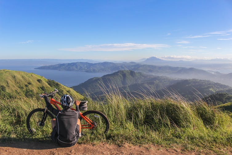 A man sitting next to his bike, wearing a helmet.