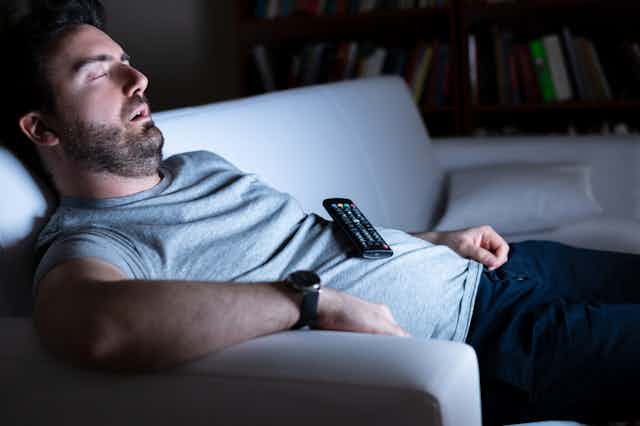 Man asleep on sofa, TV remote control resting on tummy