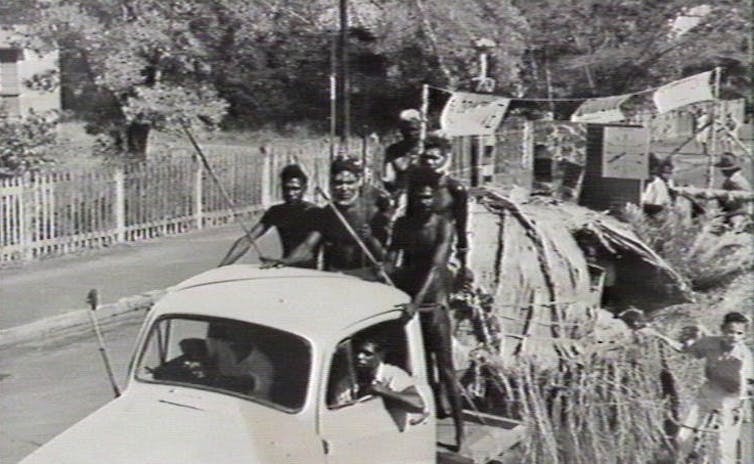 Aboriginal dancers on a float depicting a bark and grass dwelling