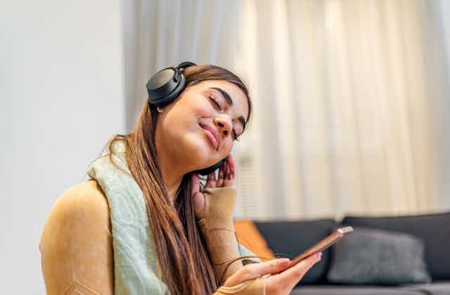 Young woman wearing headphones holding smartphone listening or humming to music 