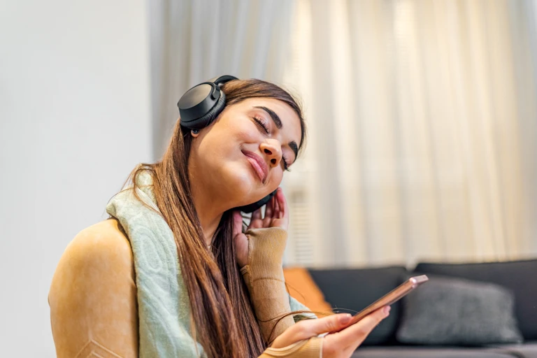 Young woman wearing headphones holding smartphone listening or humming to music