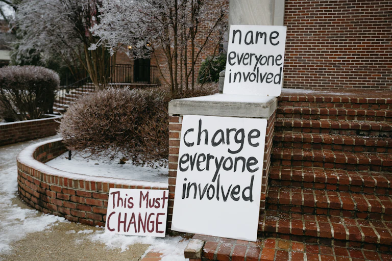 Three hand-written signs calling for action rest on a brick stair structure.