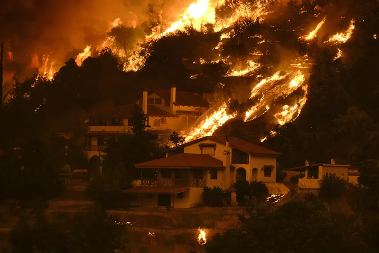 A raging wildfire spreads across a hillside and houses in Greece.