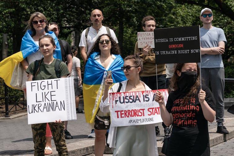 Protesters wrap themselves in a Ukrainian flag and hold signs that say 'Fight like Ukrainian' and 'Russia is a terrorist state'