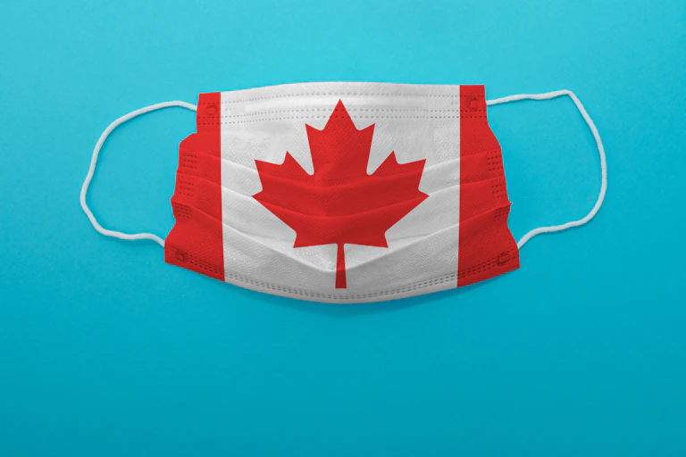 A surgical mask imprinted with the Canadian flag, against a blue background