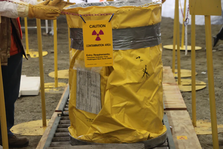 A large drum wrapped in yellow shielding behind a warning sign reading "Contamination Area" a