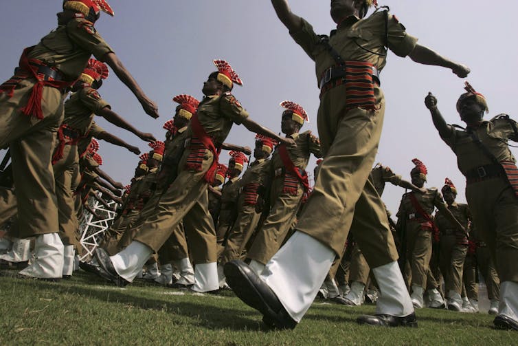 Soldiers in colourful uniforms and head gear march in unison.