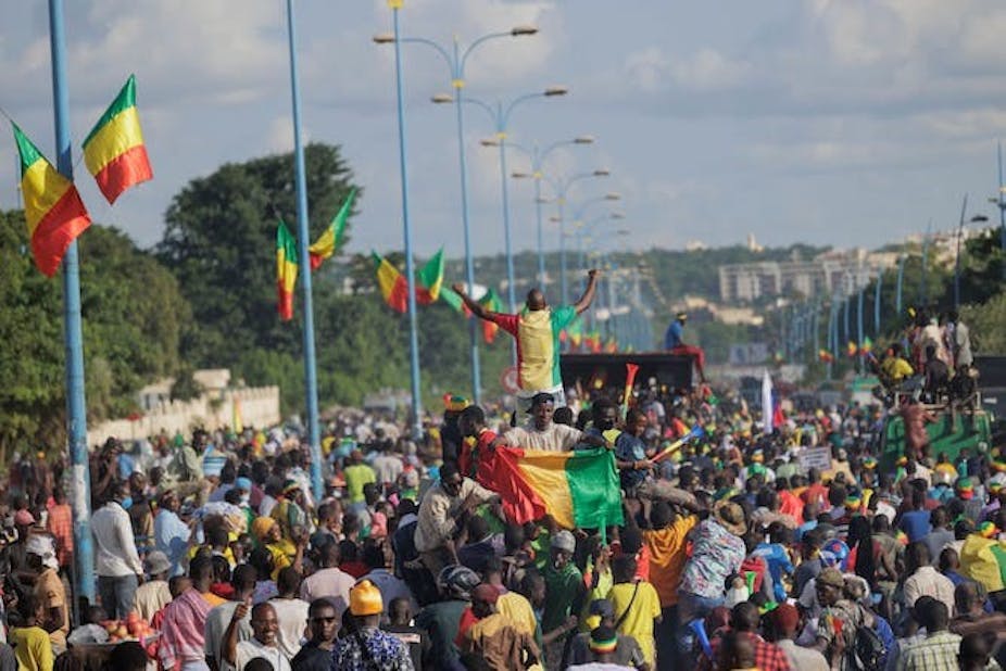 Une fouleUne foule de personnes rassemblées dans une rue et brandissant des drapeaux à bandes vertes, jaunes et rouges.