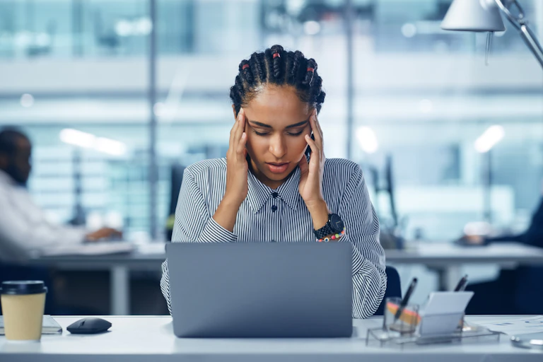 Woman in open-plan office holding fingers to her temples.