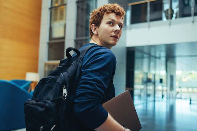 A student looks over his shoulder, carrying a laptop.