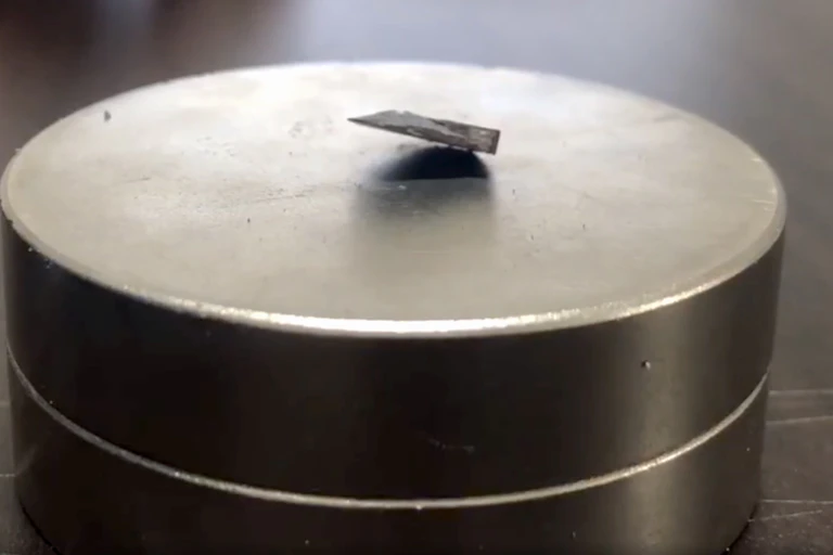 A photo showing a chip of dark material partially floating above a silver metallic magnet.