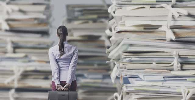Composite image showing woman with briefcase, dwarfed by stacks of paper
