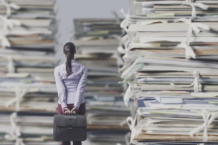 Composite image showing woman with briefcase, dwarfed by stacks of paper