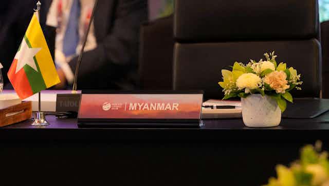 A nameplate with Myanmar inscribed on it sits on a table in front of an empty chair.