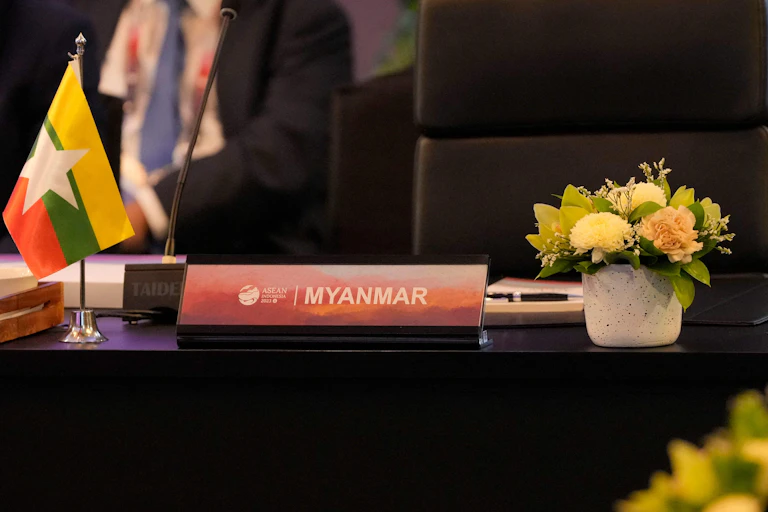 A nameplate with Myanmar inscribed on it sits on a table in front of an empty chair.