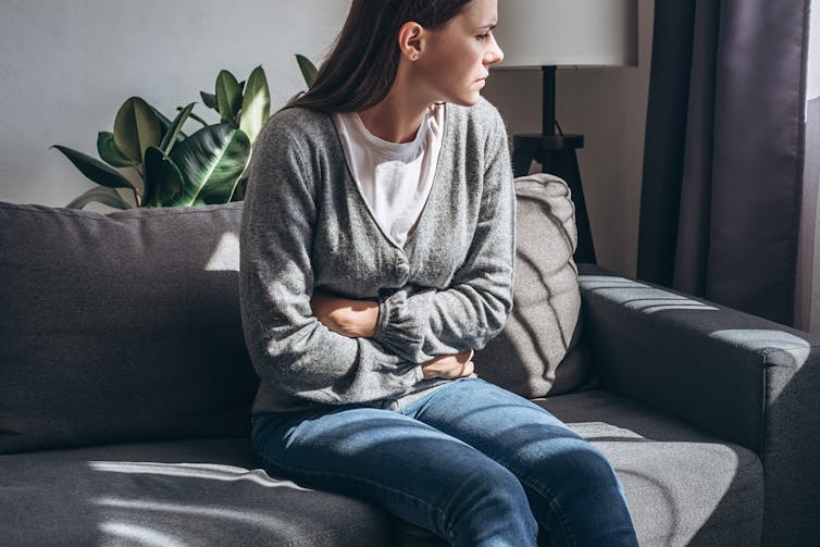 A woman sitting on a couch holds her stomach in pain.