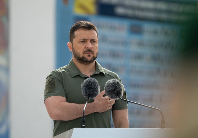 Ukrainian president Volodymyr Zelensky stands at a podium holding a clenched fist over his heart.