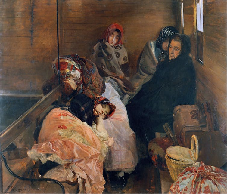 In a train compartment, several women dressed as peasants rest under the gaze of an elderly lady who watches them, dressed in black.