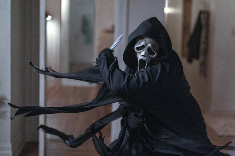 Figure in black hooded robe and scream mask slashing with a knife in an apartment.