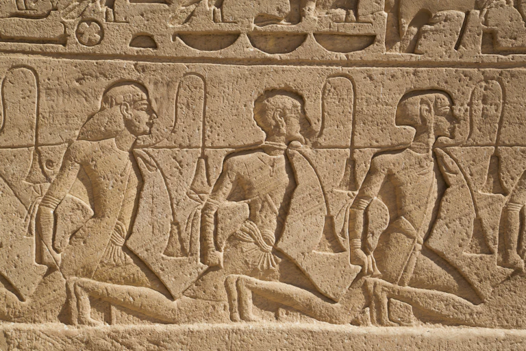 An engraving in a tan rock shows the heads and torsos of three people with ropes around their necks connecting them.