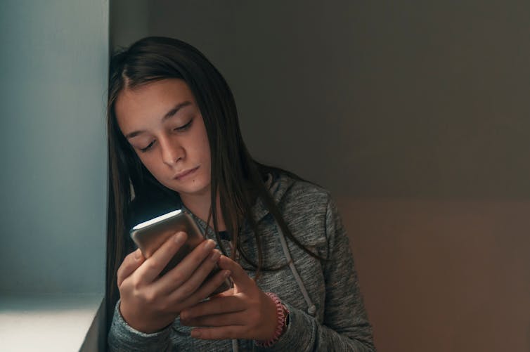 A young woman looks at a phone with an upset look.