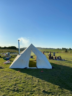 A peaked tent seen outdoors on grass against a blue sky.