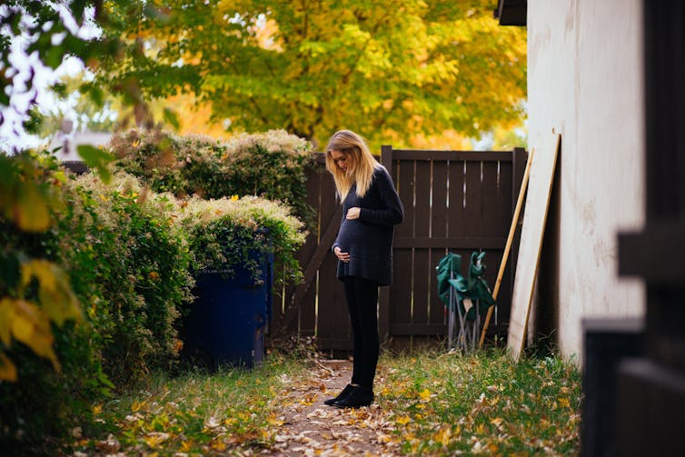 Woman standing in garden looking at her pregnant belly.