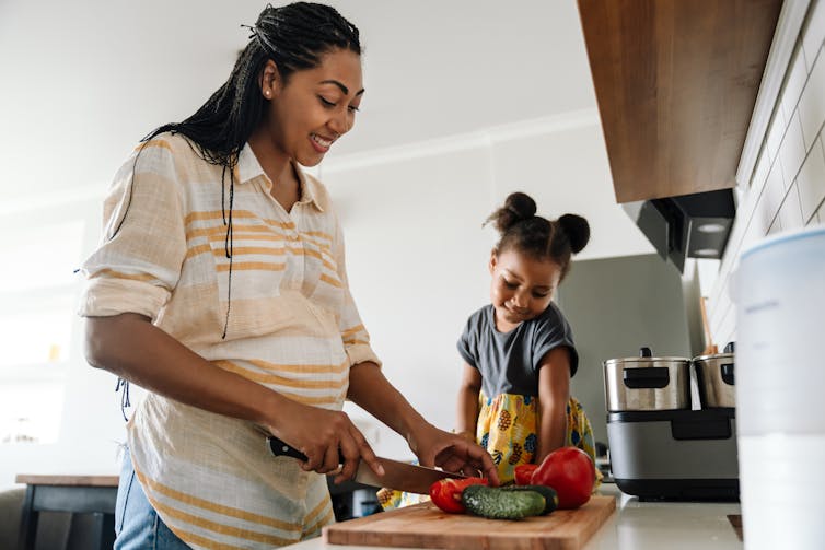 A pregnant woman cooks dinner with her baby.