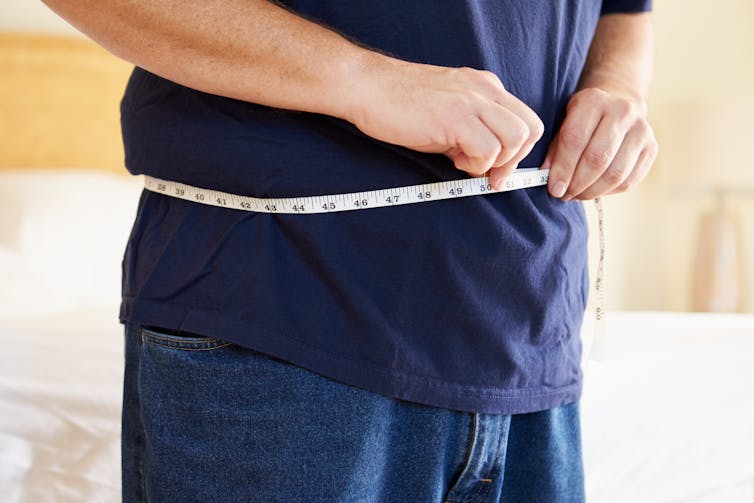 man measures own waist with tape measure