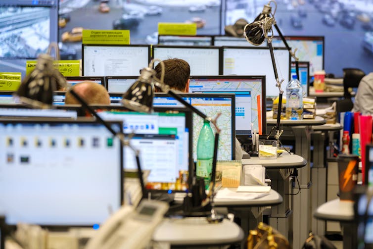 View of desks and screens in a crowded open-plan office.