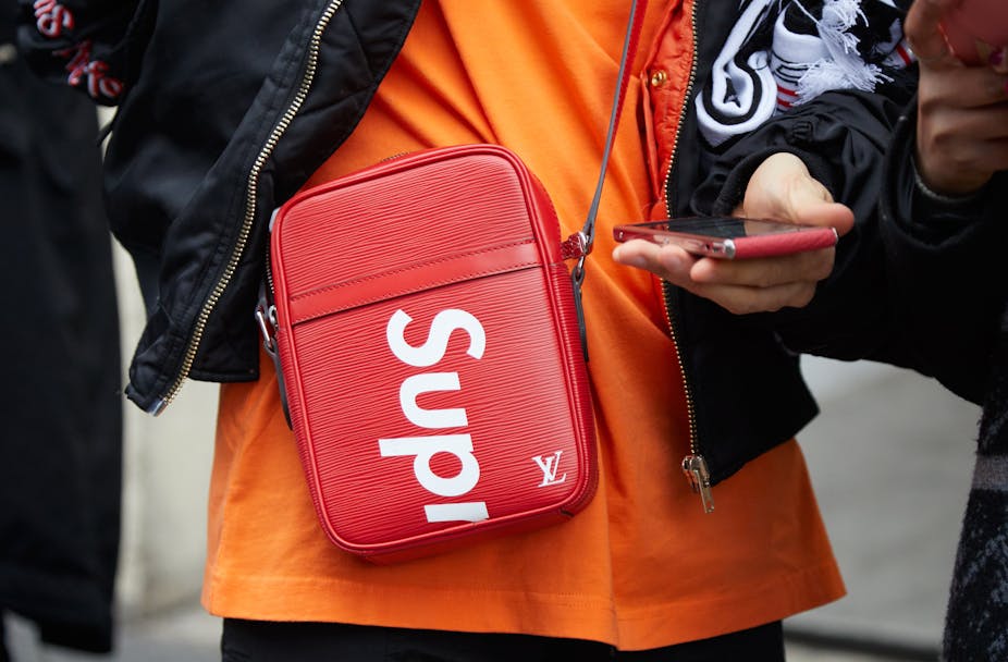 Woman wearing red Louis Vuitton crossover bag showing Supreme streetwear label.