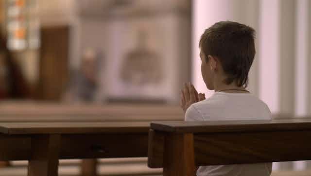 Boy sits praying on a church pew