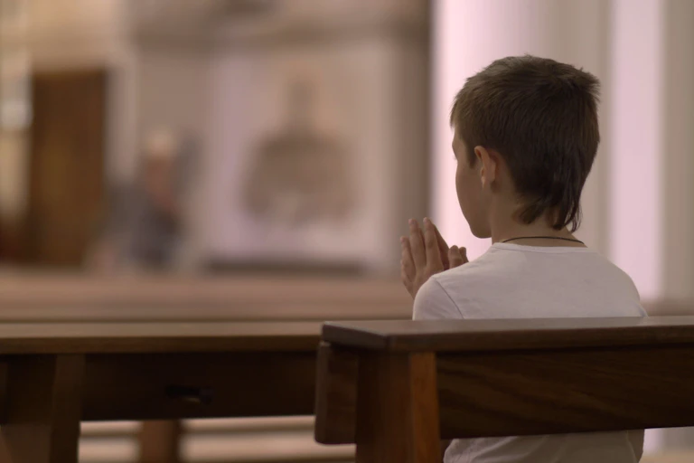 Boy sits praying on a church pew