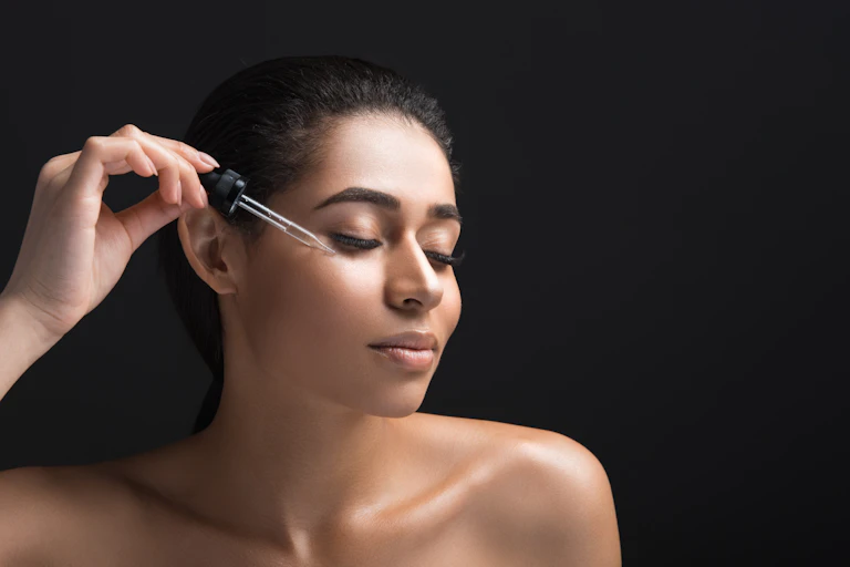A woman applying a liquid to her face using a small dropper.