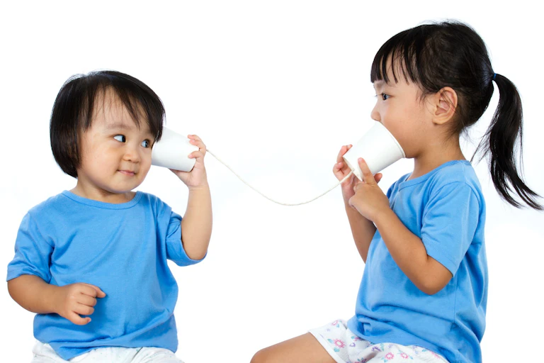 Two girls talking through a couple of cups and a rope.