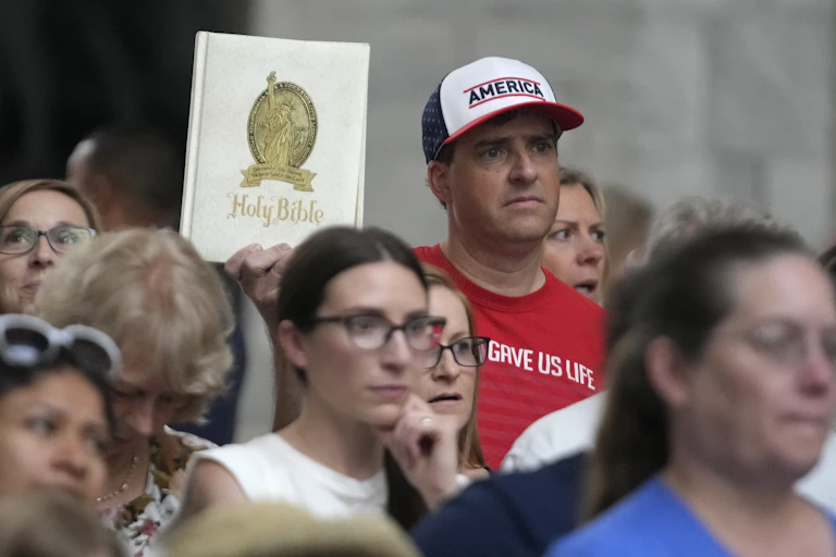 A group of people stand, with one holding a copy of the Bible.