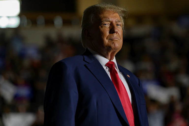 A man in a blue jacket, white shirt and red tie with a determined look.