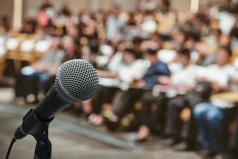 Microphone in the forefront of a blurred photo of conference hall or seminar room with people in the background