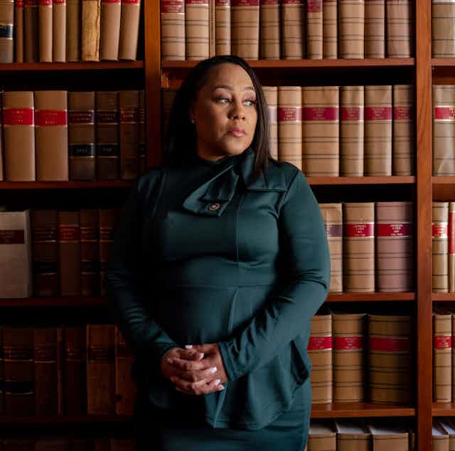 A Black woman stands in front of book shelves filled with law books.