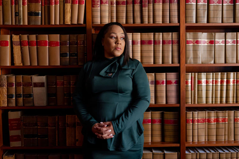A Black woman stands in front of book shelves filled with law books.