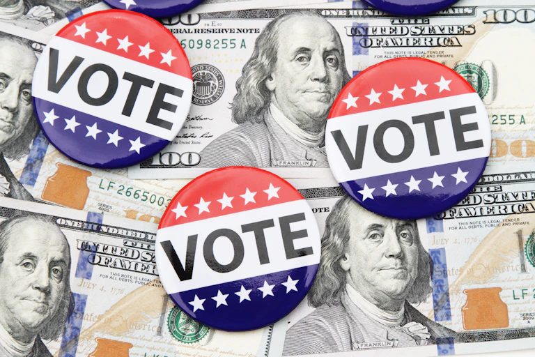 Vote buttons are laid out over 100 dollar bills with Benjamin Franklin's face on them.