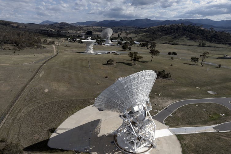 A photo showing several radio dishes on a grassy landscape with hill in the distance.
