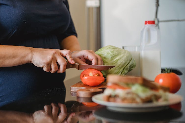 Woman cuts tomato at bench