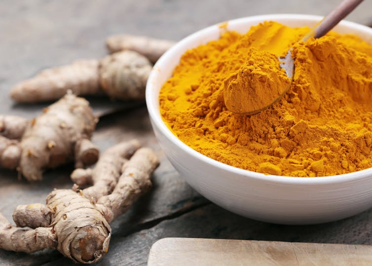 Bowl of yellow turmeric spice and roots on bench