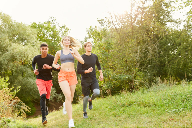 Two men and a woman go for a run in a park.